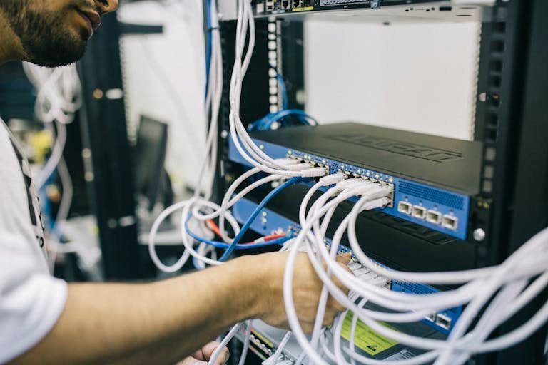 An IT professional configuring network cables in a server rack, focusing on Ethernet connections.