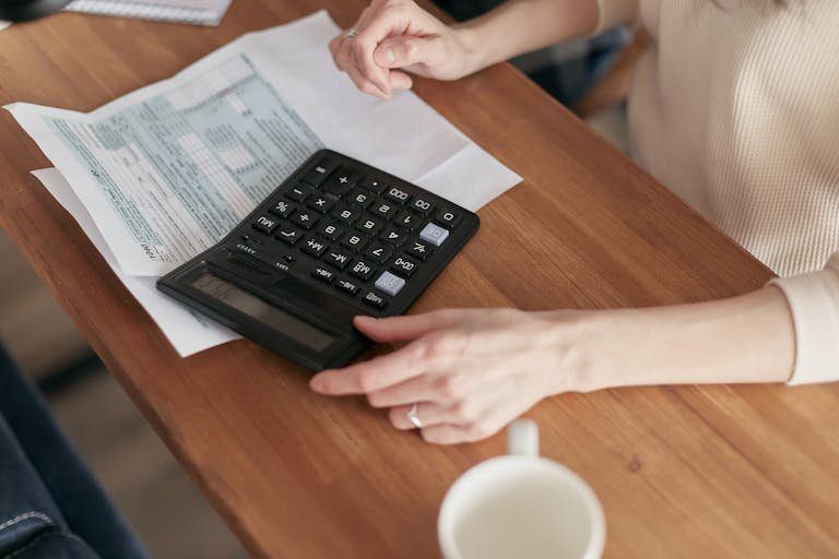 Focused individual using calculator to manage personal finances at wooden desk.