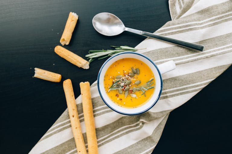 Warm pumpkin soup garnished with seeds and herbs, served with breadsticks. Perfect for a cozy meal.